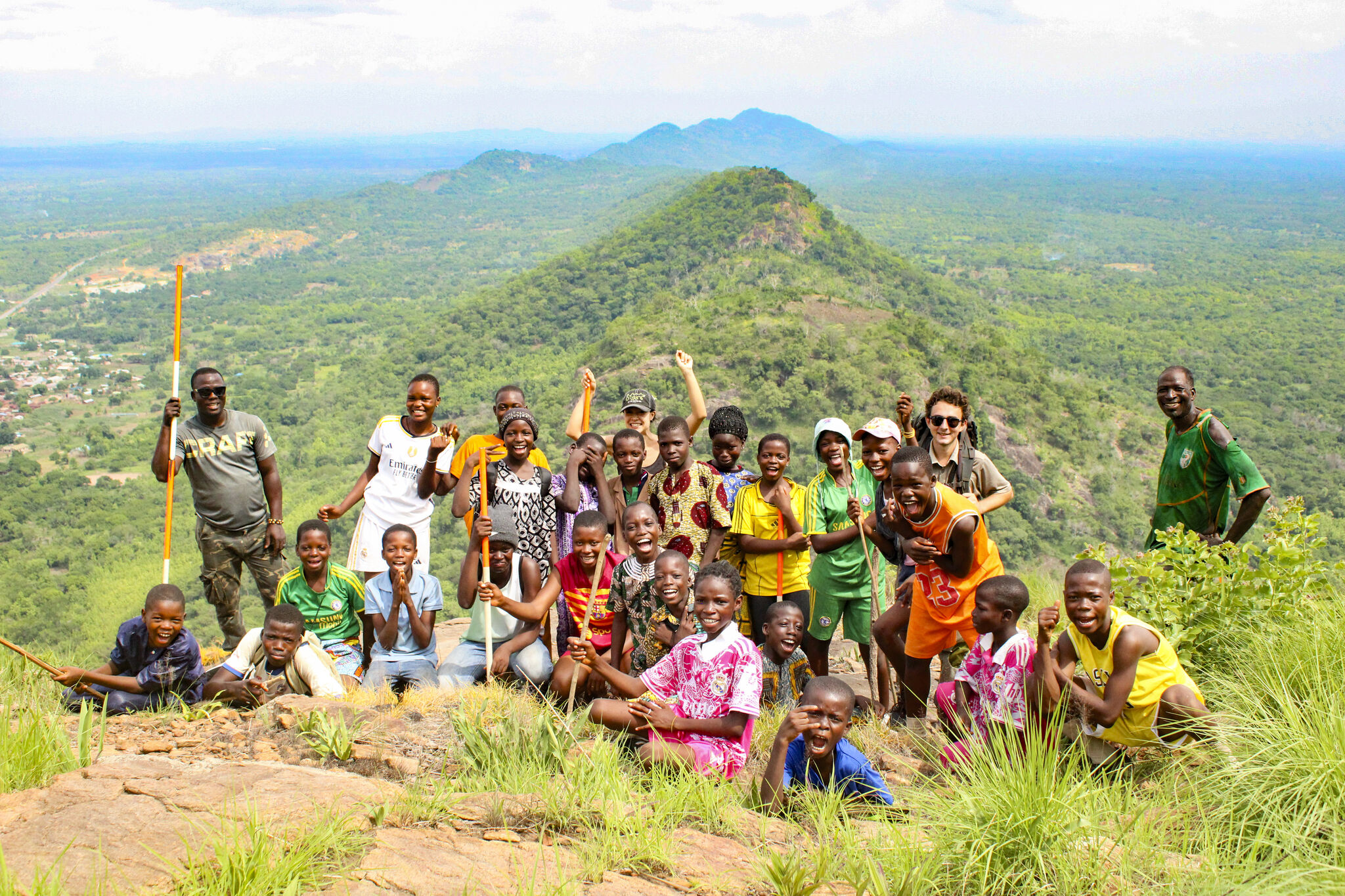 A group gathers on top of a mountain and smiles for the camera while wearing colorful clothing